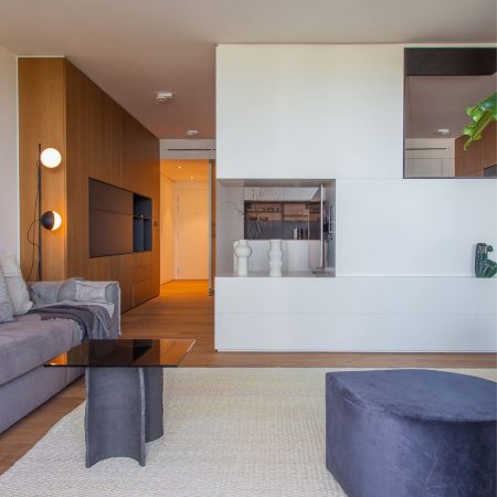 Reforma de Apartamento Moderno Llull por YLAB Arquitectos - Sala Integrada, parede azul, painel de madeirae sofá cinza