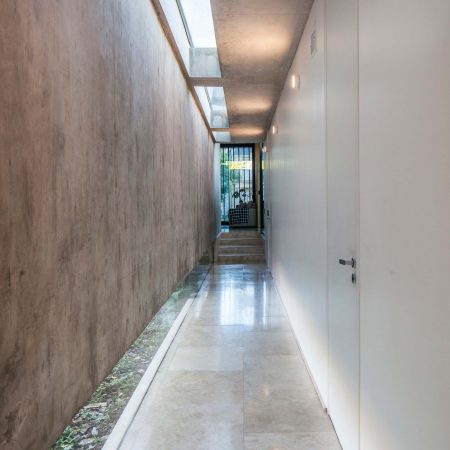 Residência BT Estudio Jorgelina Tortorici Arq, corredor com piso de concreto, parede de concreto, iluminação zenital e janela em fita no piso.