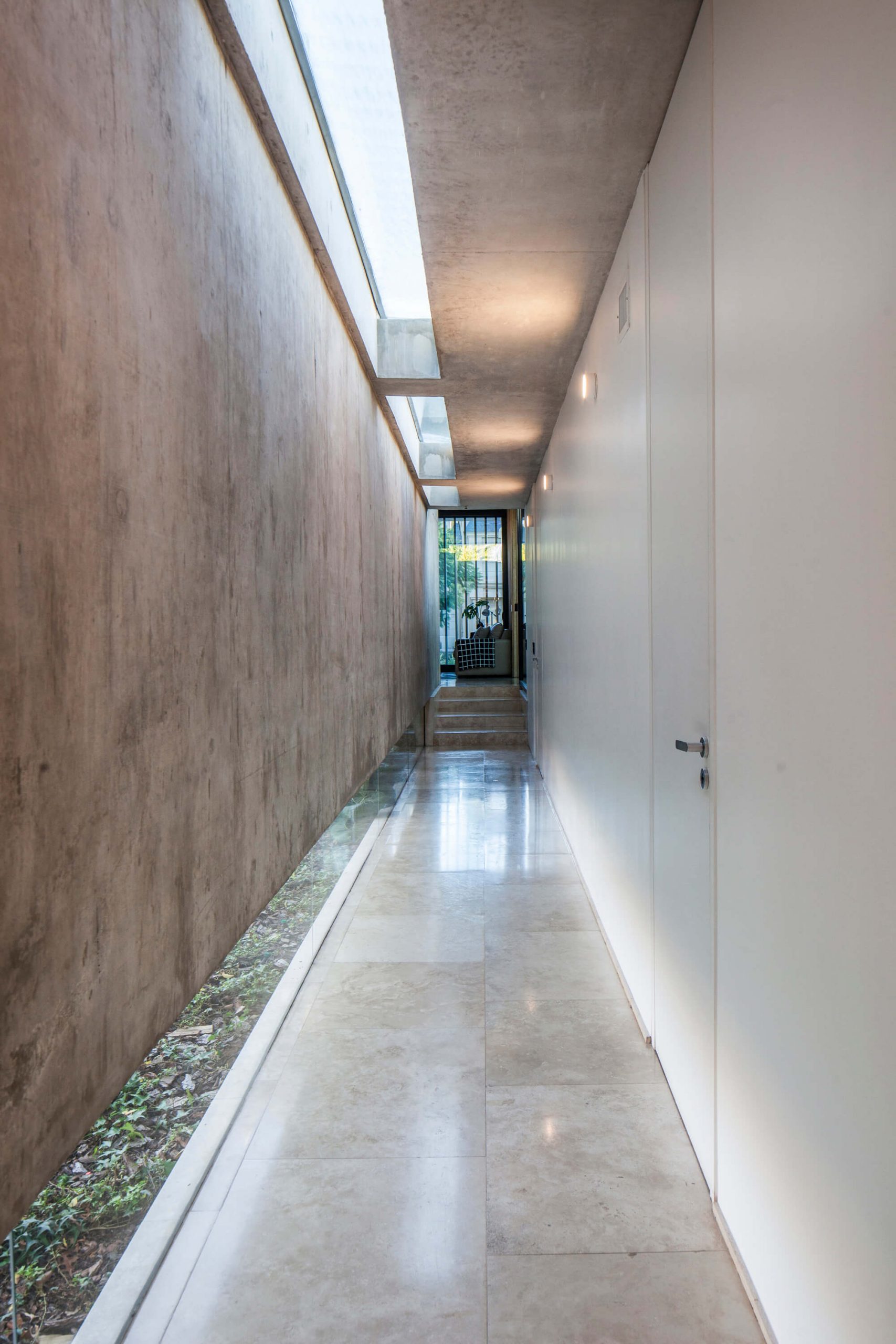 Residência BT Estudio Jorgelina Tortorici Arq, corredor com piso de concreto, parede de concreto, iluminação zenital e janela em fita no piso.