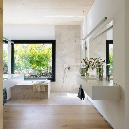 Banheiro com banheira, piso de madeira e janela grande para o jardim.