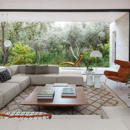 Casa Proyecto CH - Espanha. Sala de estar com sofa grande e cinza, tapete bege com preto, laje de concreto aparente e portas grandes do piso ao teto com vista para a natureza.