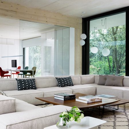 Casa Proyecto CH - Espanha. Sala de estar com sofa grande e cinza, tapete bege com preto, laje de concreto aparente e janelas grandes.