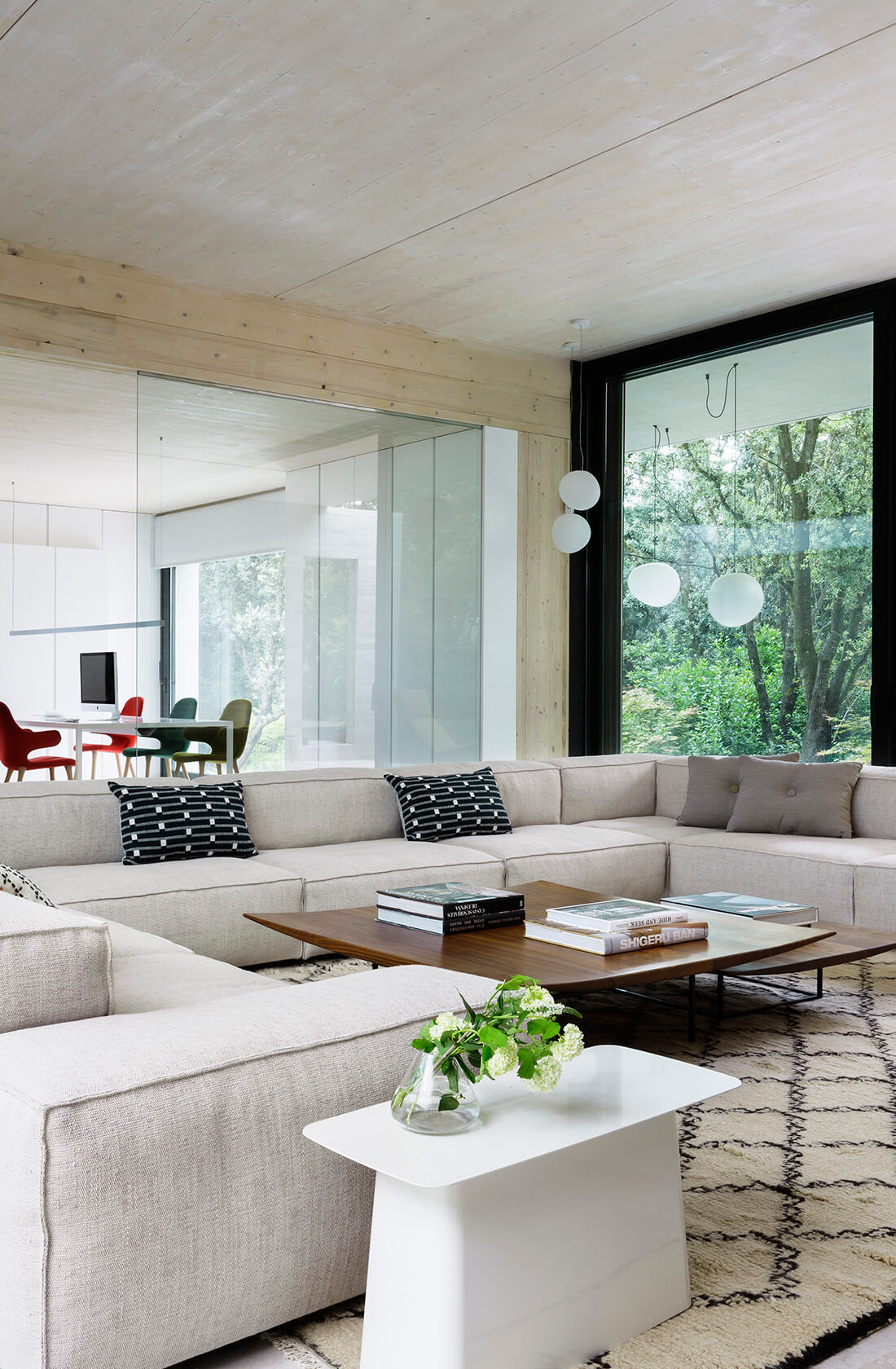Casa Proyecto CH - Espanha. Sala de estar com sofa grande e cinza, tapete bege com preto, laje de concreto aparente e janelas grandes.